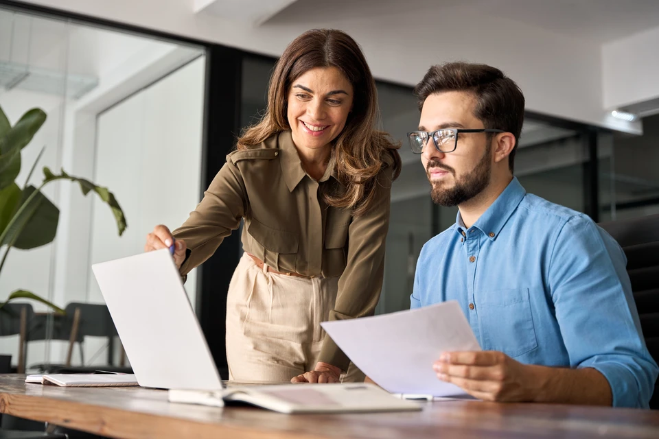 Une femme d'affaires d'un âge moyen et professionnelle explique le webinaire d'apprentissage en ligne des logiciels d'entreprise qui aide les jeunes employés au travail à regarder l'ordinateur