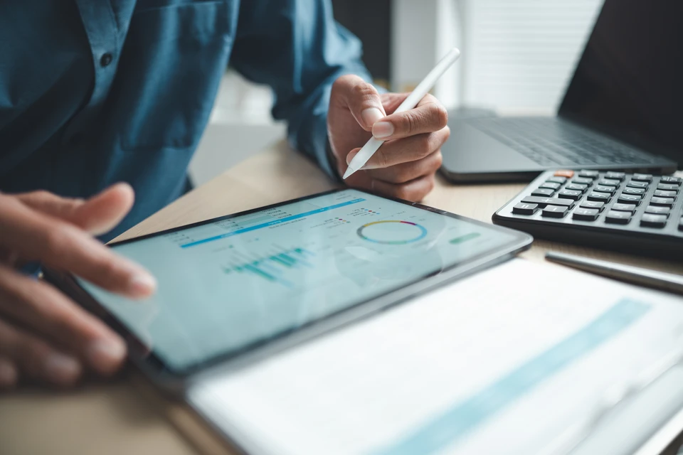 Réunion d'équipe autour d'une table en bois avec plusieurs professionnels analysant des rapports financiers, graphiques et tableaux de bord